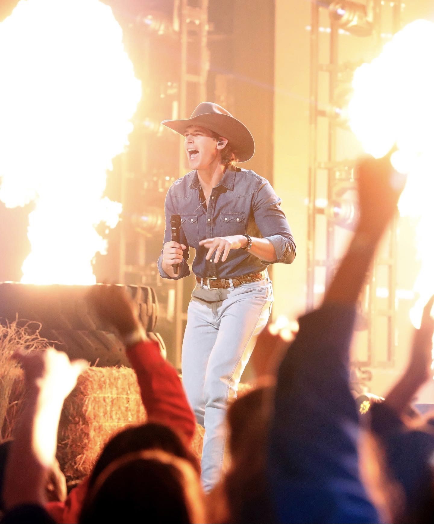 Jonah singing on a big stage in a cowboy hat with flames behind him and hands raised in the crowd