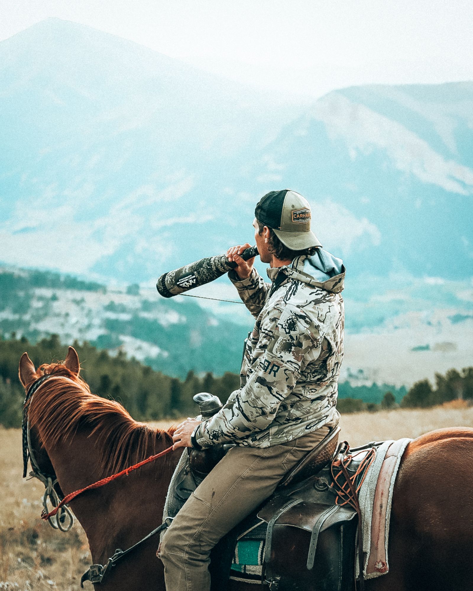 Jonah on horseback blowing an elk bugle toward a mountain